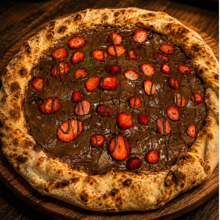 Pizza doce coberta de chocolate e morangos cortados ao meio, vista de cima.